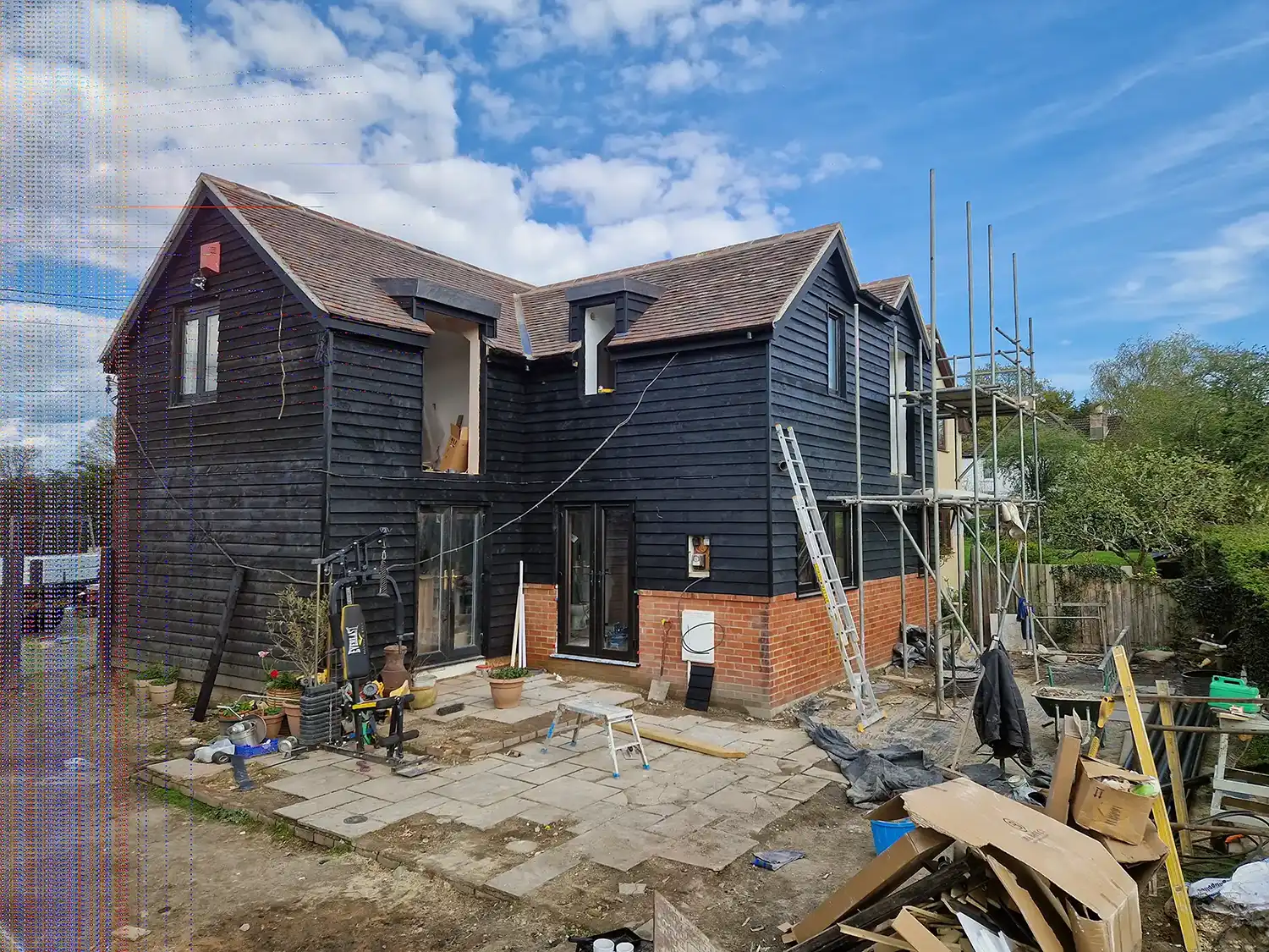 House under construction with black wooden siding, brick base, scaffolding, and construction materials outside.