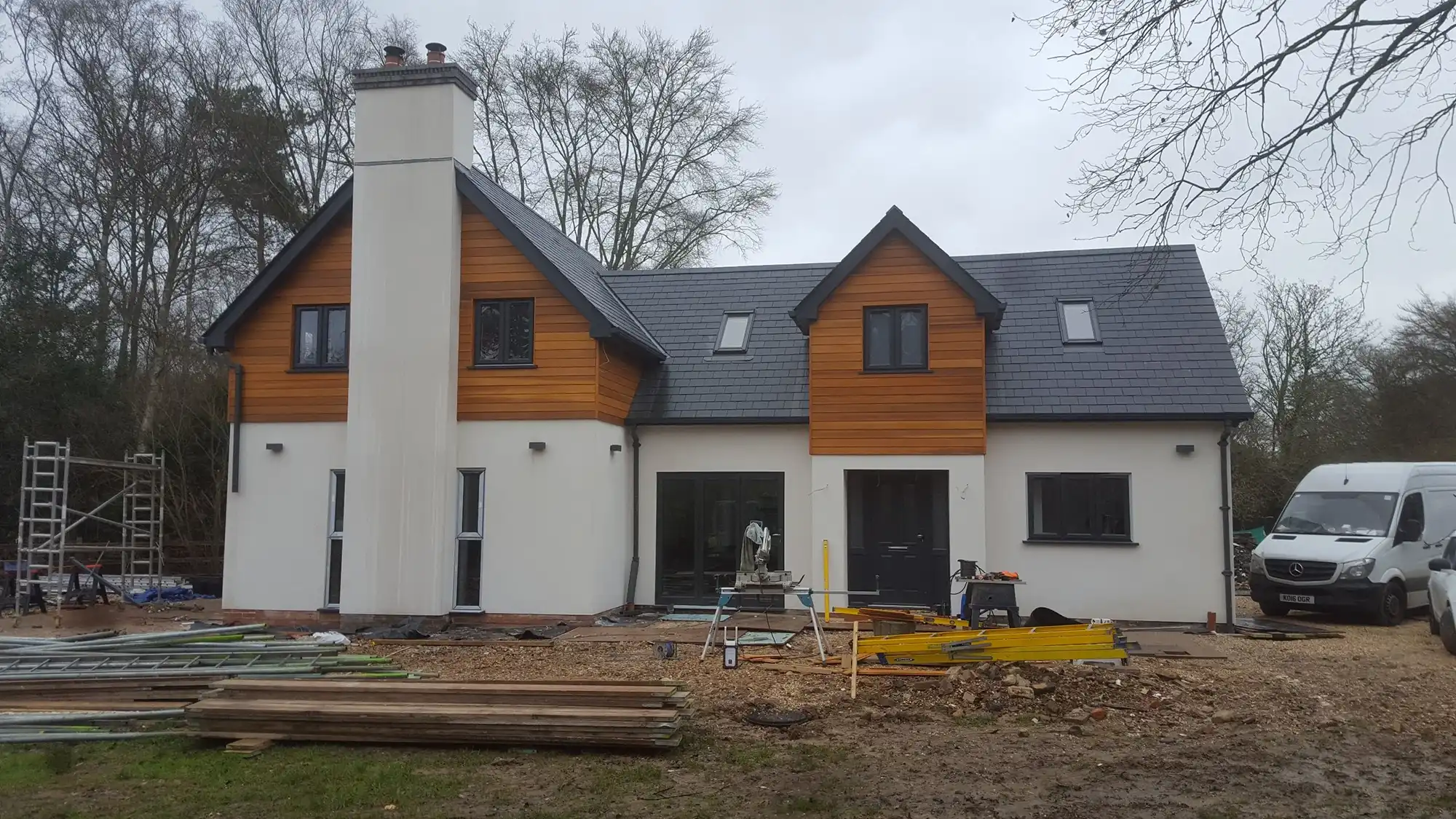 Modern two-story house with wood paneling and construction materials in the front garden.